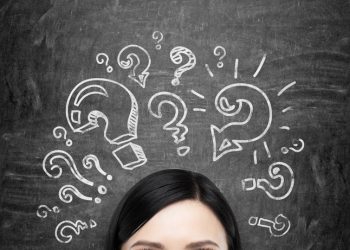 A forehead of the brunette girl who is pondering about unsolved problems. Question marks are drawn around the head. black chalkboard background.